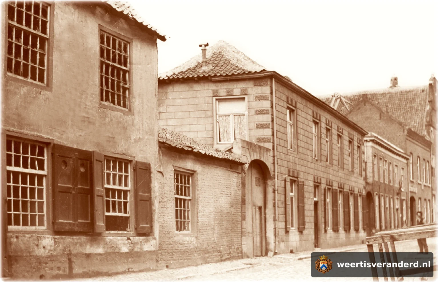 Het pand links op de foto is het hoekhuis op de Markt waar nu speelgoedzaak Bart Smit gevestigd is. Rechts naast de grote poort was het woonhuis van de familie van der Velden, weer rechts daarvan was apotheek Kneepkens (later aan de Langpoo