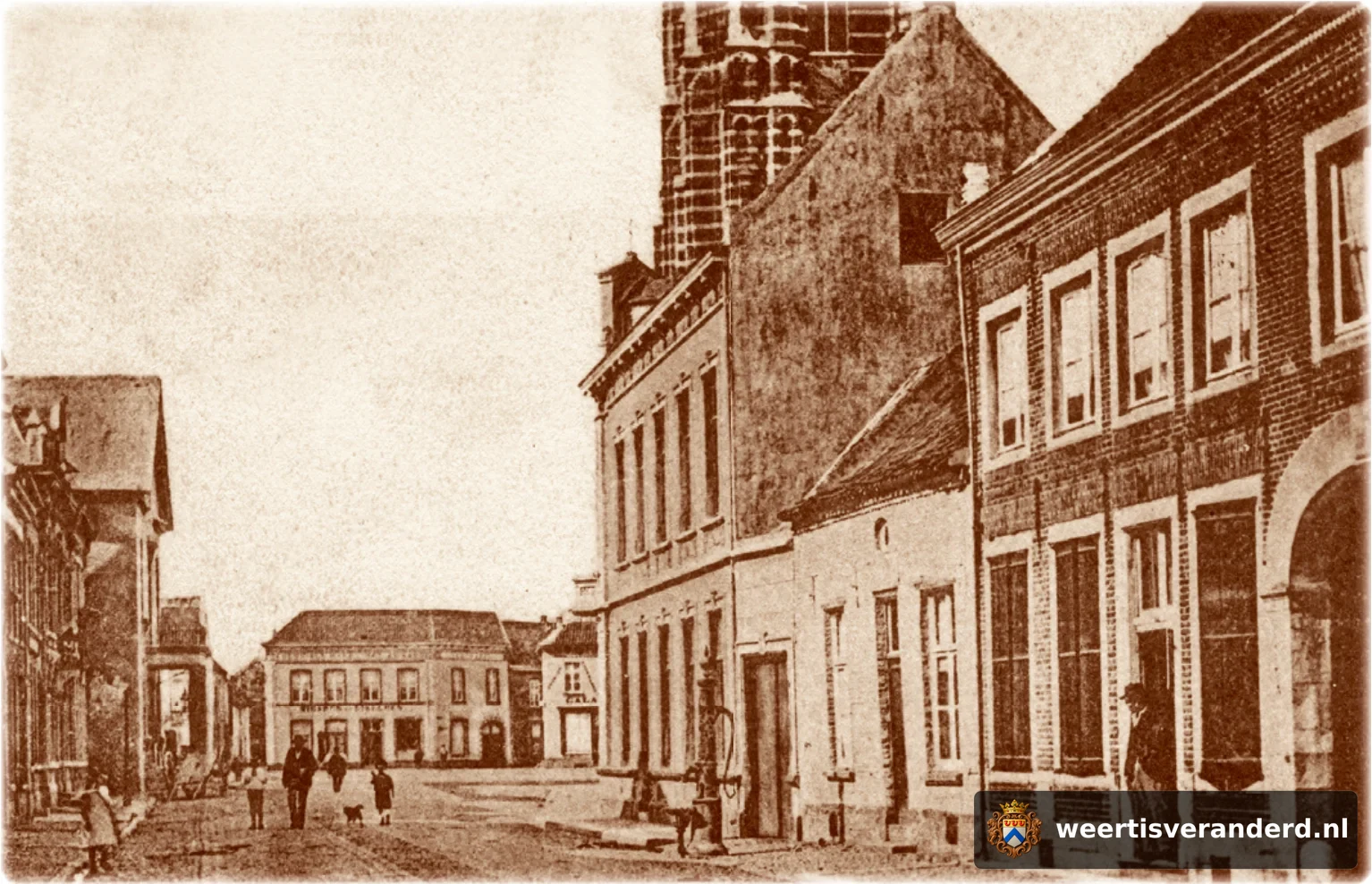 Vanuit de Langstraat kijken we richting Markt. Rechts langs de straat zien we nog een gietijzeren stadspomp.