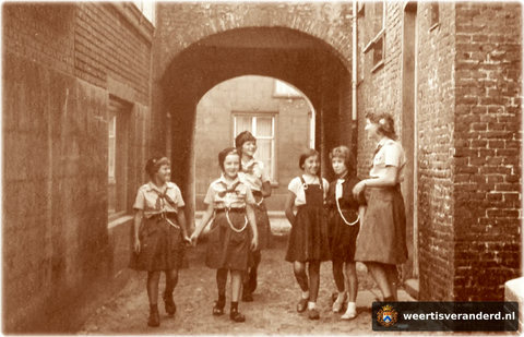 “Akela, wij doen ons best”. Een vrolijk onderonsje van gidsen (vrouwelijke verkenners) in de Gasthuissteeg. De gidsen hadden een onderkomen in het Oud Gesticht.