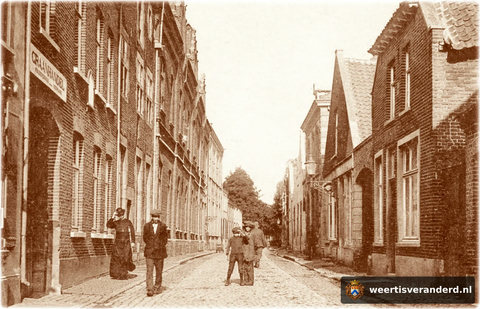 Links, met het heiligenbeeldje in de gevel, het pand van Hendriks. Daarnaast het Muntgebouw met daarachter het Bischoppelijk College. Op de stoep loopt professor Houben van het College. In het huis rechts met de lantaarn woonde de familie G