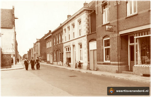 Drie muzikanten van de harmonie op weg naar een serenade. Links zien we de ingang van de Nieuwe Markt. Aan de rechterkant staat eerst het winkelpand van woninginrichting Stienen, dan de naaimachinezaak van Nijs, het voormalige woonhuis van