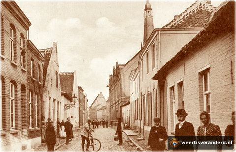 Aan de rechterkant van de foto zien we achtereenvolgens het lage huis van kapper Mies van Dooren (Mies van de Kat), het huis van de gezusters Janssen, het huis van de familie Weerts en het woonhuis van de Kleine Zusters van de Heilige Josep