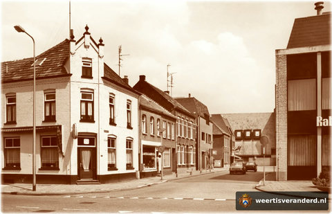 Waar eens Mies van Dooren zijn kapperszaak had, stond later de Rabobank. Hier rechts op de foto. Café De Wacht heeft een gedaanteverandering ondergaan en ernaast is een islamitisch slager gevestigd. De straat wordt op de achtergrond doorsne