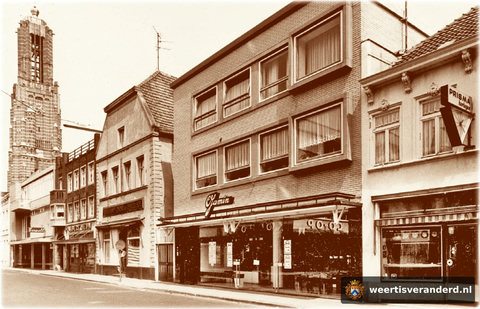 Geheel rechts op de foto horlogerie Theijs en ernaast de grote winkel van Jamin. Bakker Trienekens woonde daar weer naast. Hij staat in de deuropening met één van zijn talloze Pekineesjes, die hij fokte. In het volgende pand was toen nog Al